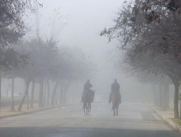 Dos agentes de la Polic&iacute;a Nacional a caballo, entre la niebla del Parque de Mar&iacute;a Luisa.

Foto: Juan Carlos Mu&ntilde;oz