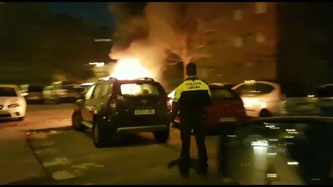 El coche siniestrado arde ante la atenta mirada de un policía local.