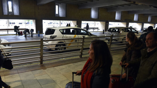 Viajeros saliendo del aeropuerto de Sevilla mientras contemplan los taxis parados para recoger pasajeros.