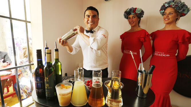 Ricardo González, bartender de FIZZ, elabora uno de los cócteles de Harveys junto a dos azafatas de Fundador en la caseta de la bodega en la Feria.
