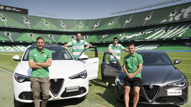oaquín, Golubovic, Saúl Blanco y Durmisi posan junto a un Alfa Romeo Stelvio y un Alfa Romeo Giulia en el césped del Estadio Benito Villamarín.