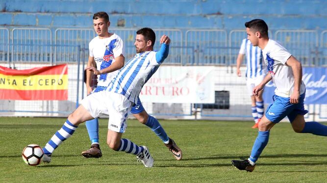 Manolo, central blanquiazul, juega atrás ante la presión de dos jugadores del Villamartín, también de blanco y azul.