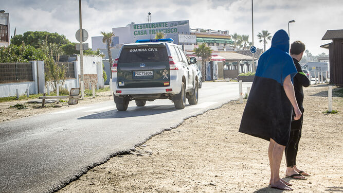 Dos surfistas observan a un vehículo de la Guardia Civil que patrulla la zona de la playa de El Palmar, ayer por la mañana.