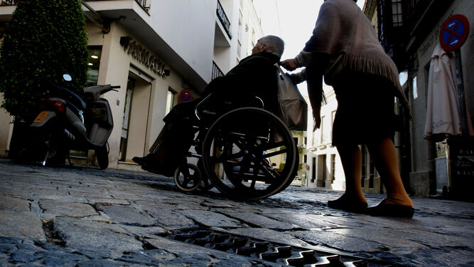 Una mujer lleva la silla de ruedas de una persona dependiente.