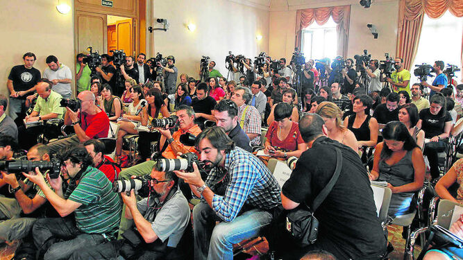 Periodistas, cámaras y fotógrafos aborrotan la sala durante una rueda de prensa.