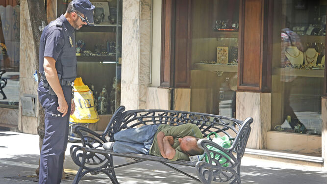 Un agente de la Policía Nacional informa a un indigente de los riesgos del calor ayer en la calle Larga.
