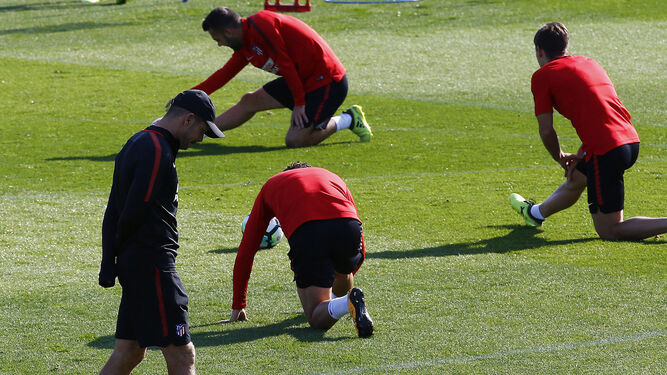 Simeone se muestra pensativo mientras dos de sus futbolistas estiran.