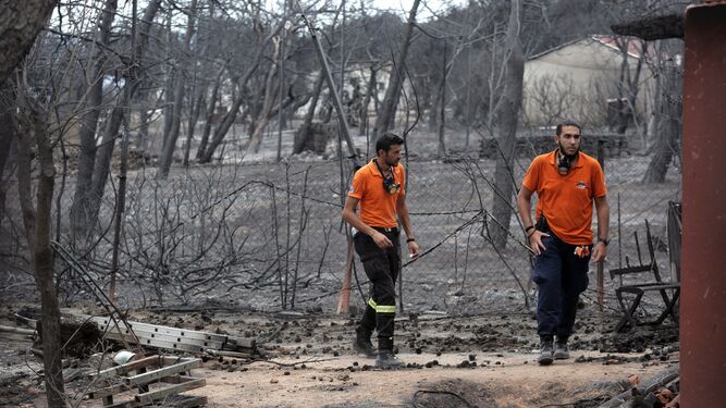 Dos miembros del personal de rescate buscan a posibles víctimas en una zona afectada, ayer en la ciudad griega de Mati.