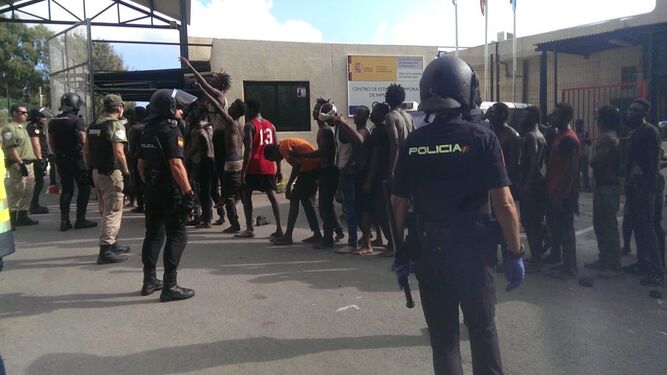 Varios de los inmigrantes, custodiados por la Policía Nacional, esperan su entrada al CETI de Ceuta.