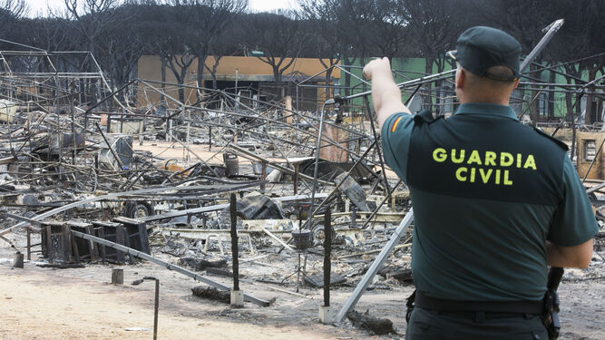 Un agente de la Guardia Civil de Huelva señala los módulos arrasados por el fuego en las instalaciones turísticas de Mazagón.
