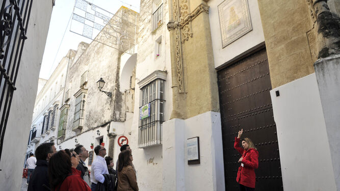 Un grupo de turistas atienden las explicaciones de una guía en una calle del conjunto monumental de Arcos.