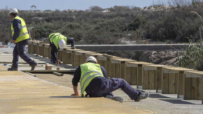 Operarios trabajando en la colocación de pasarelas y bancos en el nuevo paseo de la playa de Camposoto.