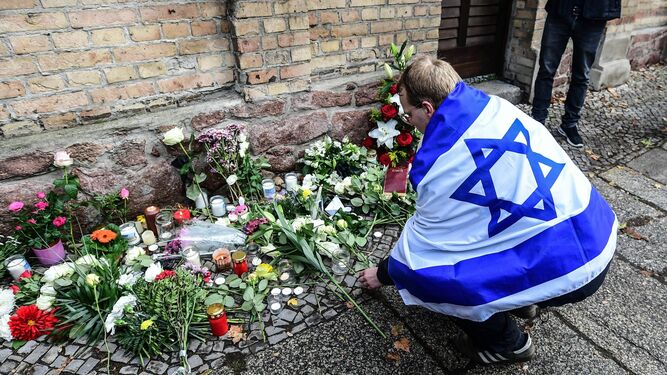 Un hombre envuelto en una bandera israelí deposita flores junto a la sinagoga de Halle, en Alemania.