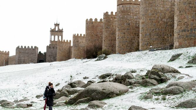 Una mujer camina junto al lienzo norte de la muralla de Ávila cubierta por una fina capa nieve.