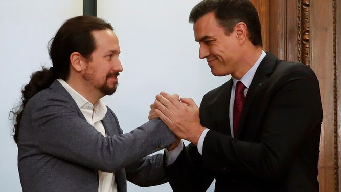 Pablo Iglesias y Pedro Sánchez estrechan sus manos tras el acuerdo de Gobierno de coalición.
