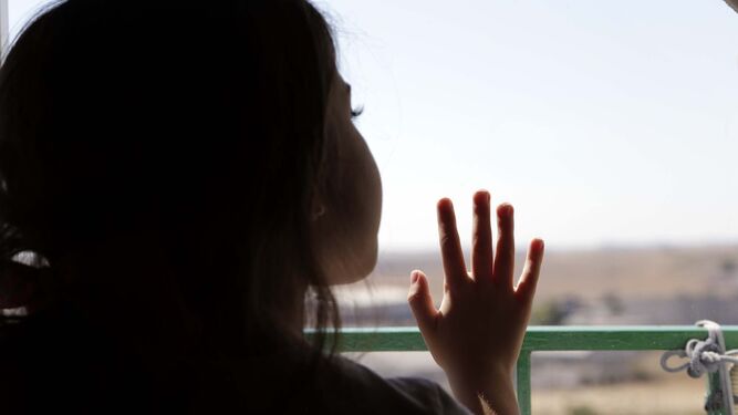 Una niña asomándose por una ventana.