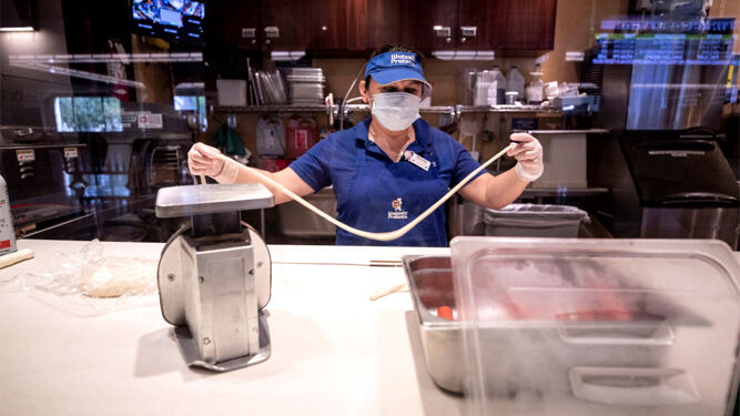 Una trabajadora de un restaurante de Los Ángeles manipula alimentos protegida con guantes y mascarilla.