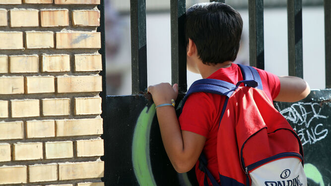 Un niño mira, a través de la cancela, el patio de un colegio.