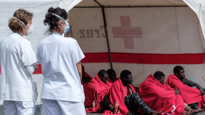 Dos sanitarias ante ante algunos de los inmigrantes subsaharianos rescatados este domingo en Gran Canaria.