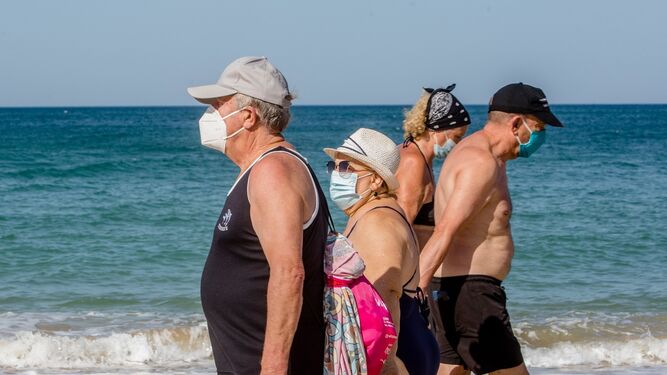 Personas mayores paseando por la playa con sus mascarillas.
