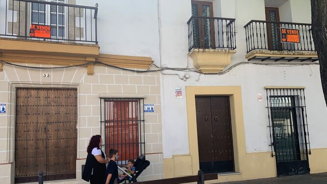 Una mujer pasea en compañía de dos niños junto a dos viviendas a la venta en Jerez.