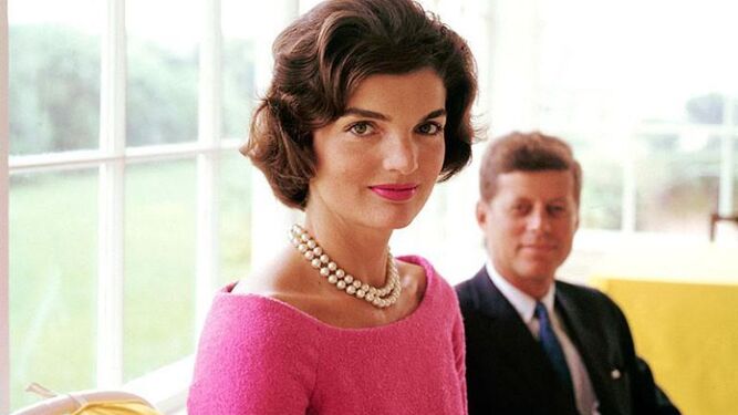 Jackeline Kennedy (JFK en segundo plano), con vestido fucsia y collar de perlas.