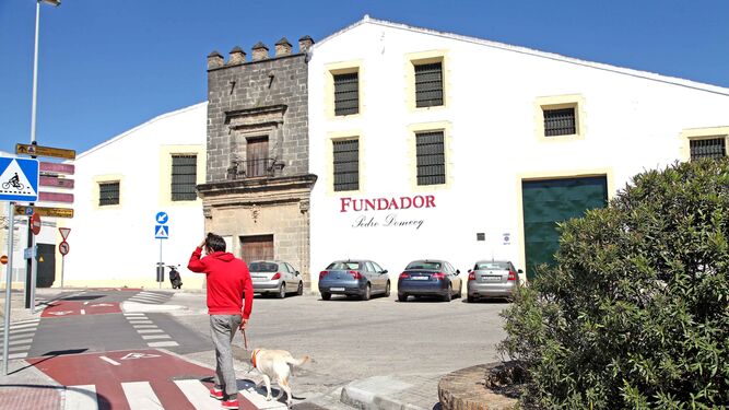 Un ciudadano pasea a su perro junto a la sede en Jerez de Bodegas Fundador, del Grupo Emperador.