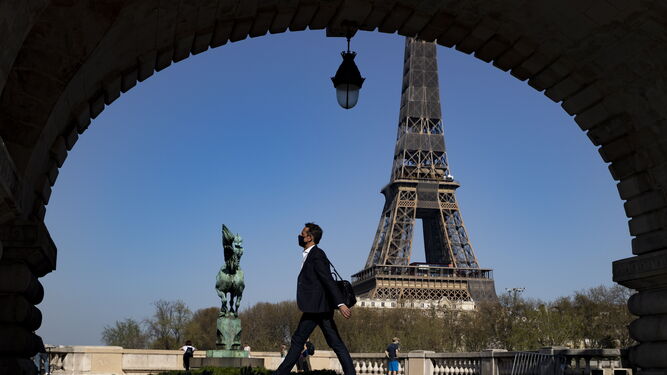 Un hombre con mascarilla pasea ante la Torre Eiffel, en París.