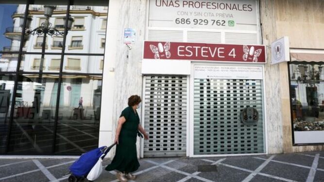 Una mujer pasa con el carro de la compra por delante de un comercio del centro cerrado durante la pandemia.