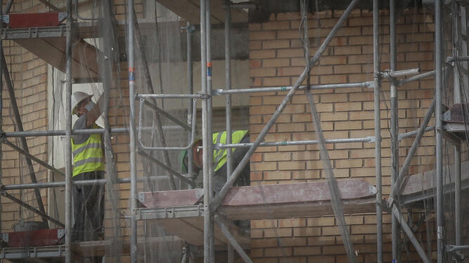 Trabajadores de la construcción junto a un andamio en una obra de un edificio.