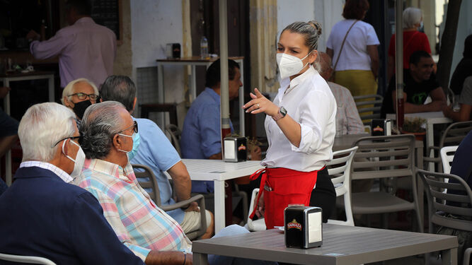 Una camarera conversa con unos clientes, todos con la mascarilla puesta, en la terraza de un bar.