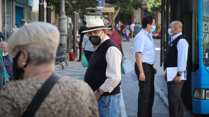 Ciudadanos con la mascarilla puesta junto a una parada de autobús urbano.