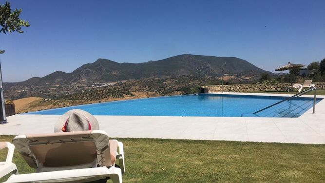 Una persona disfruta de las flamantes instalaciones de la piscina del Hotel Los Tadeos, en Zahara de la Sierra, con un paisaje de suaves montañas al fondo.