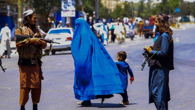 Una mujer afgana atraviesa una calle de Kabul  con dos talibanes armados.