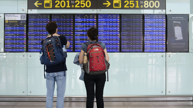 Dos pasajeros, ante los paneles de información de vuelos en el aeropuerto del Prat de Barcelona.