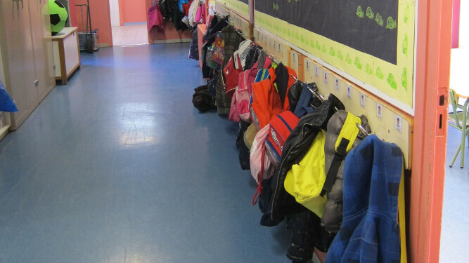 Un pasillo de colegio, con maletas colgadas en percheros
