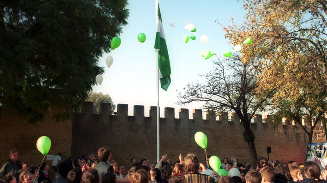 Un grupo de escolares iza la bandera de Andalucía.