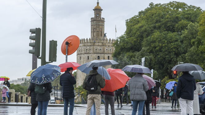 Varias personas se refugian debajo de sus paraguas, en Sevilla.