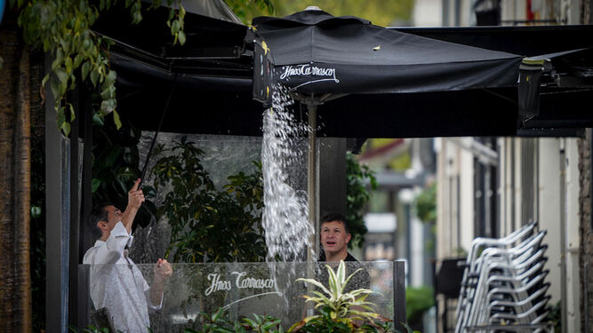 Un camarero achicando agua del toldo de un restaurante de la avenida Caballero Bonald
