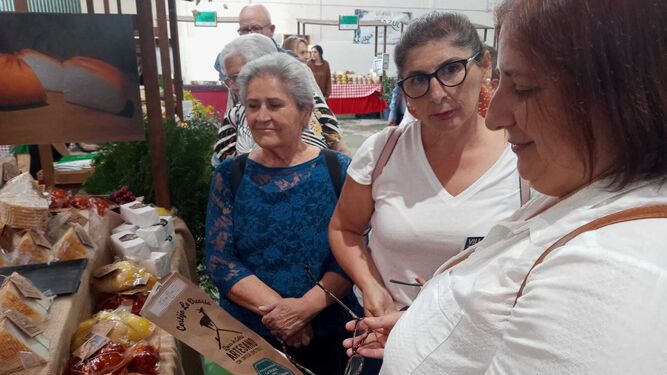 Varias mujeres visitando uno de los expositores  en la apertura de la Feria del Queso de Villaluenga