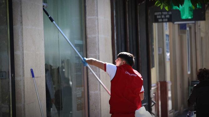 Un trabjador limpia los cristales del escaparate de una tienda del centro de Jerez.