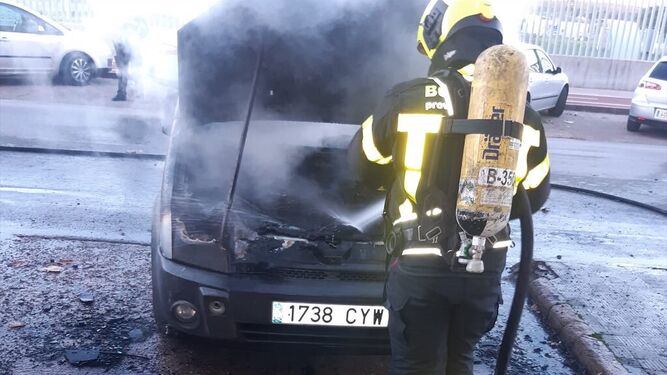 Un bombero tratando de apagar el fuego originado en un vehículo.