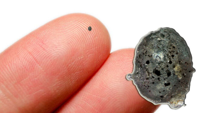 Detalle del micrometeorito ampliado, y con su tamaño real, sobre un dedo