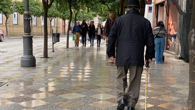 Una persona mayor pasea por la calle Larga con ayuda de un bastón.