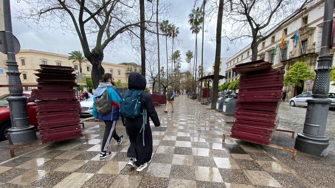 Peatones pasean por Cristina junto a las estructuras de los palcos de Semana Santa en un día de lluvia.
